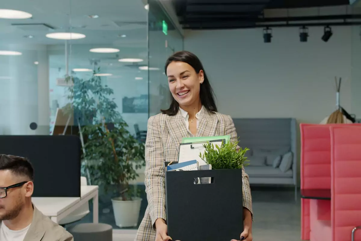 Eine Mitarbeiterin trägt einen Karton und eine Pflanze durch ein modernes Büro