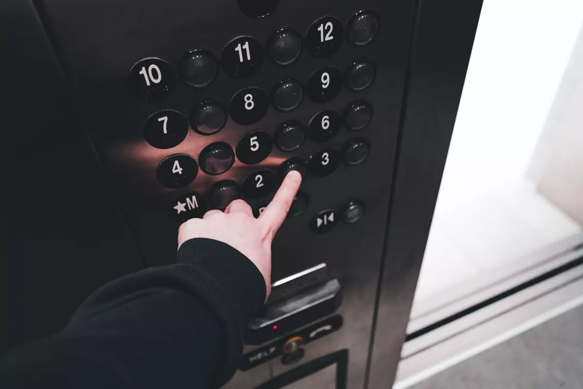 Eine Hand wählt eine Etage am Bedienfeld eines Aufzugs