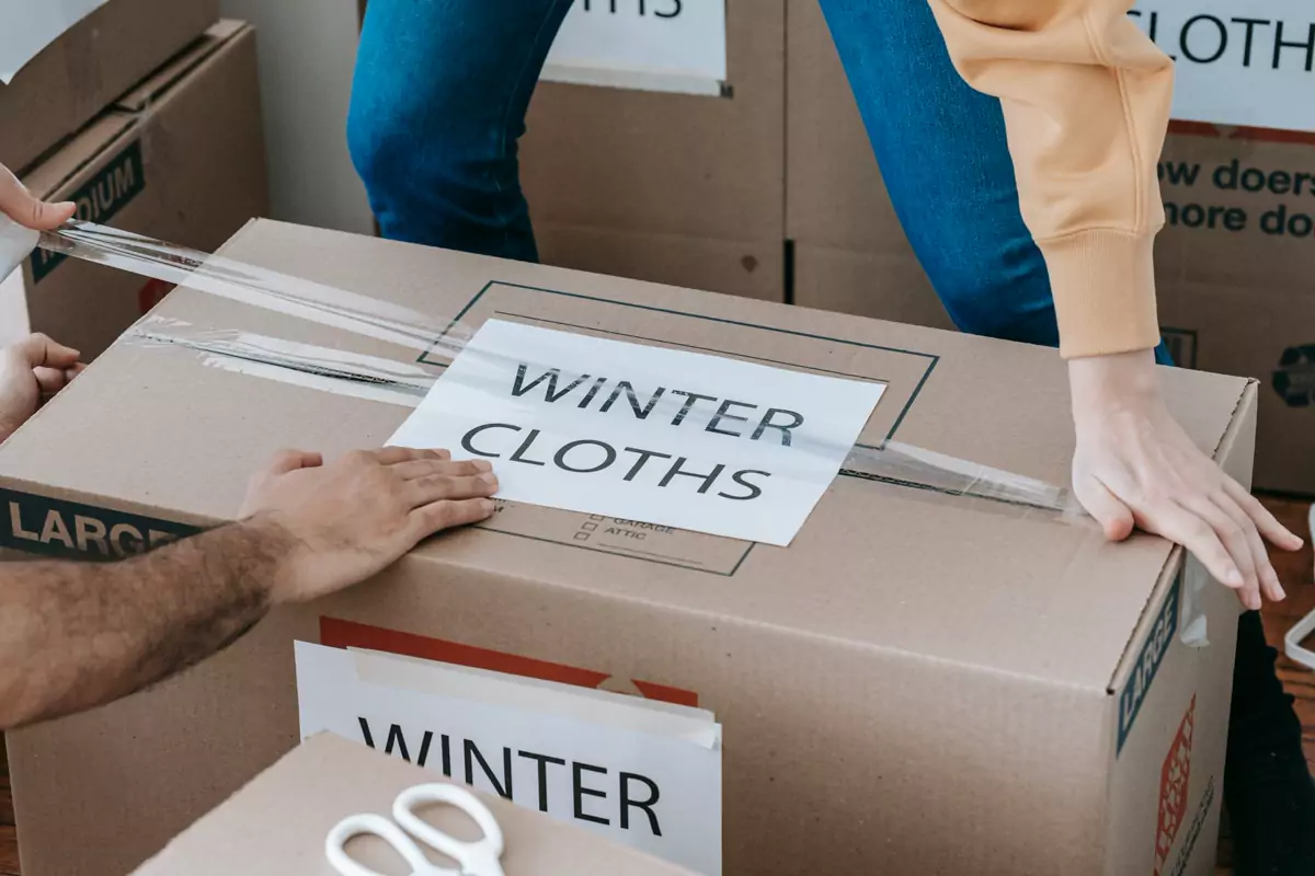 Hände packen Kleidung geordnet in einen beschrifteten Karton