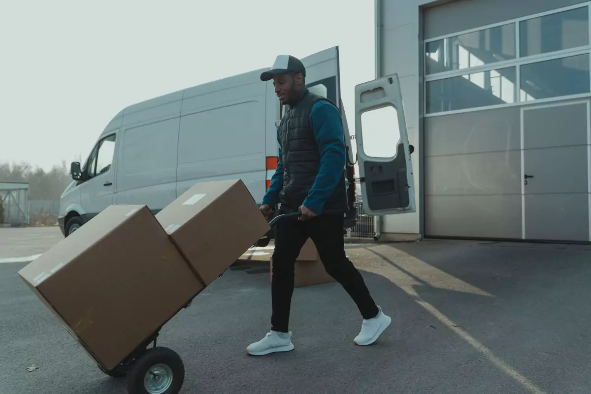 Ein Helfer schiebt Kartons auf einem Rollwagen zu einem Transporter