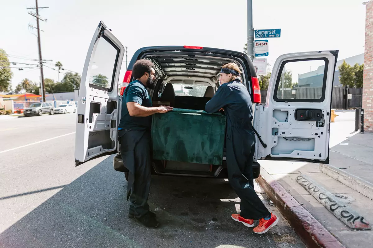 Zwei Helfer laden ein Sofa am Straßenrand in einen Transporter