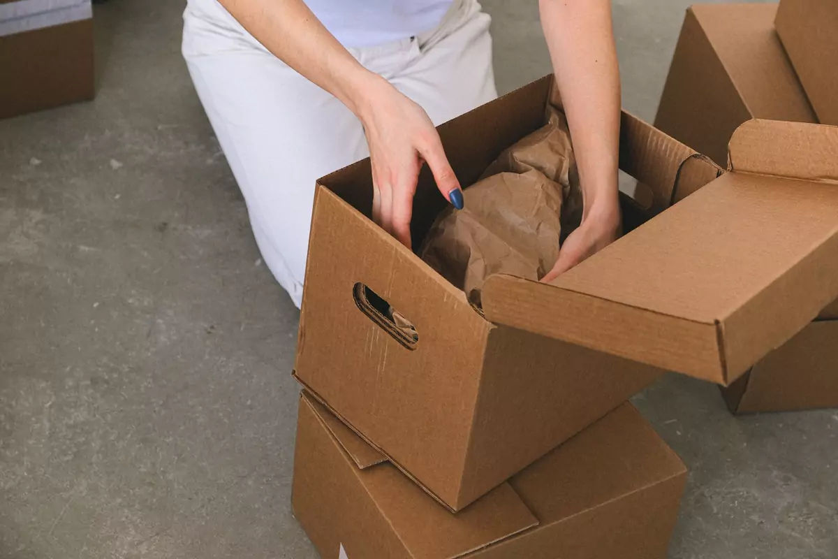 Hände legen sorgfältig verpackte Gegenstände in einen Umzugskarton