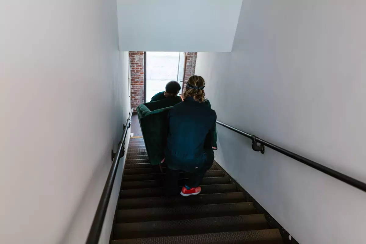 Zwei Umzugshelfer tragen ein Sofa vorsichtig über eine Treppe