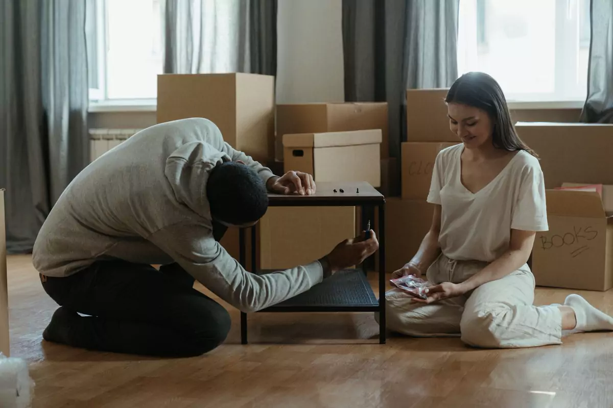 Zwei Personen montieren einen Tisch zwischen gepackten Kartons