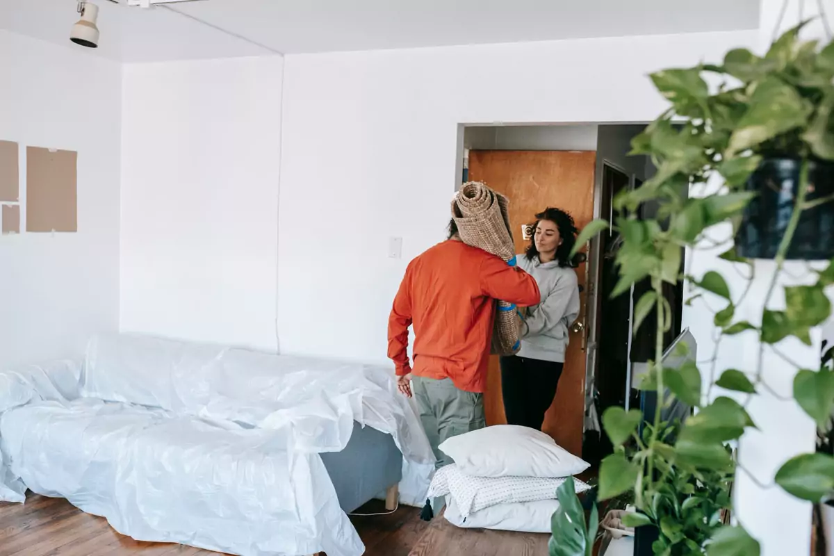Ein Mann trägt einen zusammengerollten Teppich durch eine Wohnung
