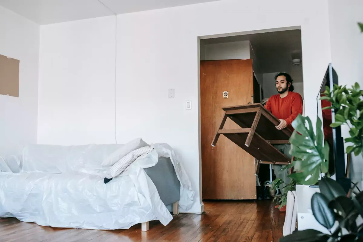 Ein Mann trägt einen Holztisch durch eine Wohnung