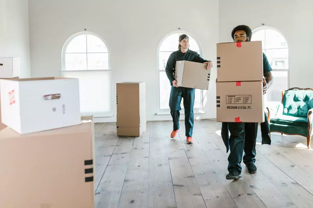Zwei Umzugshelfer tragen Kartons durch einen hellen Wohnraum