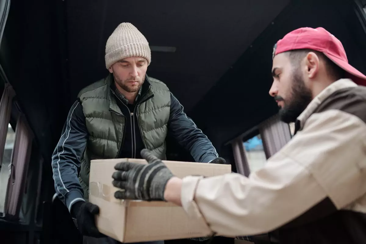 Zwei Helfer heben gemeinsam einen großen Karton aus einem Transporter